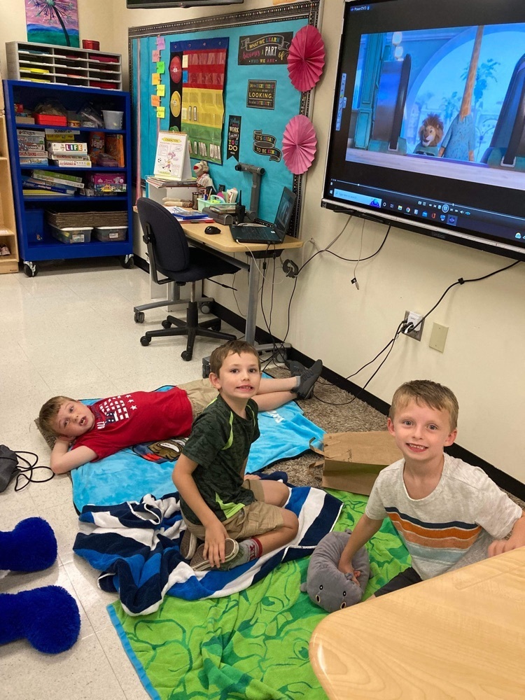 3 students sitting with blankets on classroom floor